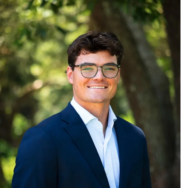 Howell Polk, smiling, outdoors in a blazer and glasses